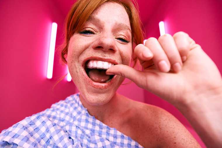 [CRO] Woman - Ginger - Checkered shirt - Looking down - Freckles - Smile - Aligner - Hand - Pink - Light - Background - Desktop